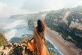 woman in flowing kaftan admiring view from a cliff over the beach