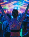 A woman with fluorescent bodypainting seen from back in a music event, dancing in neon color lights