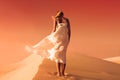 Woman in fluttering dress. Desert and sand dunes. Red sky.