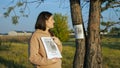 woman with flyers stack stands near poster report of missing dog with photo stuck on tree trunk