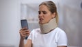 Woman in foam cervical collar reading message on cellphone, feeling pain in neck Royalty Free Stock Photo