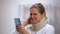 Woman in foam cervical collar reading message on phone feeling neck pain, injury Royalty Free Stock Photo