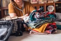 A woman folds clothes from a pile of selected belongings and puts them in luggage on the bed. Packing to go on a getaway vacation