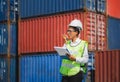 Woman Foreman in hardhat and safety vest holding holding clipboard checklist and talks on two-way radio control loading containers