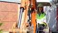 Woman foreman wearing work helmet and reflecting jacket drives an excavator at building site.