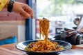 Woman with fork picking up indo chinese manchurian hakka street food noodles from a black bowl placed on a wooden table Royalty Free Stock Photo