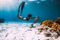 Woman free diver with fins near coral over sandy sea and sea snake