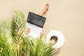 Woman freelancer with laptop sitting under coconut palm tree  branches. Female eating royal dates fruit from a bowl. Summer sand Royalty Free Stock Photo