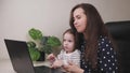 A woman freelancer with a small child in her arms is talking through a laptop monitor screen, work in a mother& x27;s home Royalty Free Stock Photo