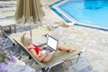 Woman freelancer, travel blogger works on a laptop. sitting on a lounger in the garden by the pool.