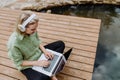 Woman, freelancer working on laptop, sitting on a pier by the backyard lake, a concept of remote office, work during Royalty Free Stock Photo