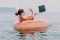 Woman freelancer works on laptop swimming in sea on pink inflatable ring. Happy tourist floating on inflatable donut and Royalty Free Stock Photo