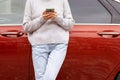 woman in front of lateral door red car in warm pullover blue jeans