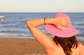 Woman with fuchsia hat on head waiting by the ocean