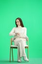 A woman, full-length, on a green background, sitting on a chair Royalty Free Stock Photo