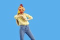 Young woman wearing funny strange chicken mask dancing on blue studio background