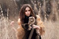 Woman in fur coat with owl on hand by first autumn snow. Beautiful brunette with long hair in nature, holding an owl. Romantic, d