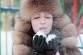 Woman in fur hat blowing snowflakes in winter