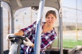 Woman gardener driving agricultural vehicle in hothouse