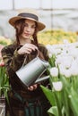 A woman gardener in a hat and gloves waters a flower bed of tulips using a watering can. Gardening hobby concept. Soft selective Royalty Free Stock Photo