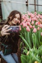 Woman gardener makes selfie. The girl smiles and uses a mobile phone in the tulip flowers greenhouse. Soft selective focus Royalty Free Stock Photo