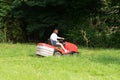 Woman gardener with red modern tractor in field garden job driving a lawn mower