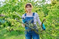 Woman gardener with saw and dry cut branches looking at camera in garden Royalty Free Stock Photo
