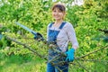 Woman gardener with saw and dry cut branches looking at camera in garden Royalty Free Stock Photo