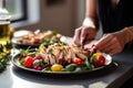 woman garnishing grilled chicken salad with olives