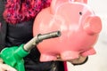 Woman at gas station holding big pink piggy bank and refueling gun in hand, concept of rising fuel prices Royalty Free Stock Photo