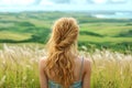 Woman gazing over green fields in summer, rear view