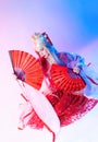 A woman in a geisha costume with fans sits on a white background