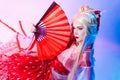 A woman in a geisha costume with fans sits on a white background