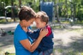 The woman gently hugs her son on the playground. The little boy is naughty and his mother calms him down