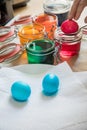 Woman getting Easter eggs with spoon of bright Easter cold colour color dye in red, orange, yellow, green, blue glass jar to dry Royalty Free Stock Photo