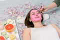 Woman getting facial care by beautician at spa salon, side view, close-up. Young beautiful girl receiving pink facial Royalty Free Stock Photo