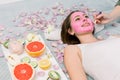 Woman getting facial care by beautician at spa salon, side view, close-up. Young beautiful girl receiving pink facial Royalty Free Stock Photo