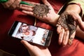 Woman getting a henna tattoo mehendi design copied from phone onto her hand for the bride bridesmaid shaadi event or a