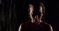 Woman is getting wet under rain in night time, rising eyes to camera and looking, water flows