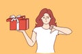 Woman with gift in hands is nervous and points finger down due to poor quality of present