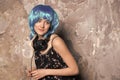 Woman in blue wig smiling with headphones on cement wall