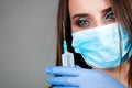 Woman or girl nurse or doctor in medical gown and protective gauze mask with sterile gloves on hands with syringe with drop from