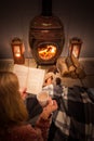 Woman girl sitting in front of a cozy fireplace during winter under a blanket  reading a book drinking coffee/hot chocolate. Royalty Free Stock Photo