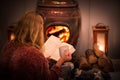 Woman girl sitting in front of a cozy fireplace during winter under a blanket reading a book drinking coffee/hot chocolate.