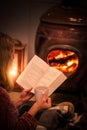 Woman girl sitting in front of a cozy fireplace during winter under a blanket reading a book drinking coffee/hot chocolate. Royalty Free Stock Photo