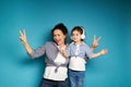 A woman and a girl wearing headphones, equally dressed singing and dancing, posing against a blue background with copy space Royalty Free Stock Photo