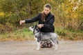 Woman gives a command to her dog puppy Siberian Husky in the autumn park. Dog training