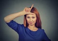 Woman giving loser sign on forehead, looking at you