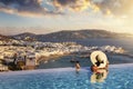 A woman with a glas of wine in a swimming pool enjoys the view over the town of Mykonos island, Greece Royalty Free Stock Photo