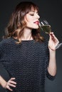 Woman with glass of champagne drinking sparkling wine on dark background. Lady with long curly hair celebrating. Portrait